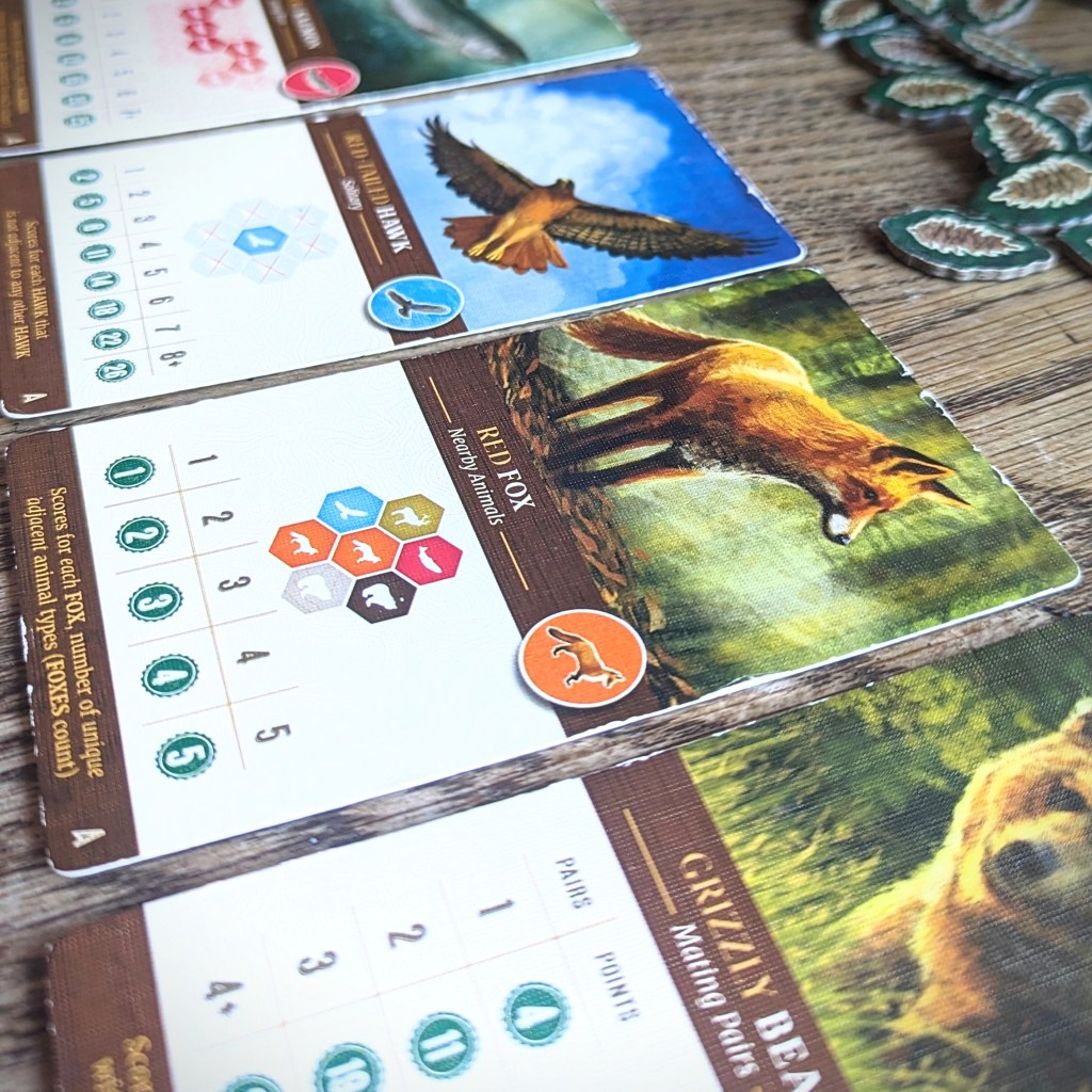 A close up photo of the Wildlife Scoring Cards. Each of them has a photo of a specific animal (e.g. a fox) and a scoring objective (e.g. the fox gets a point for each different animal that surrounds it).