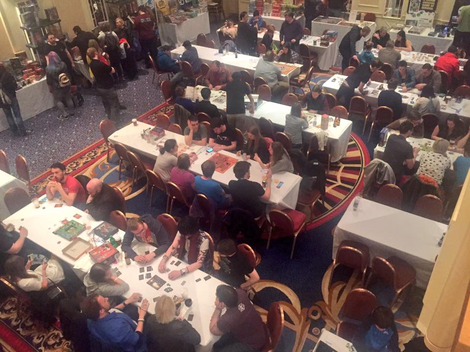 Photo showing the gaming area. There are lots of long tables full of people having a lot of gaming fun!